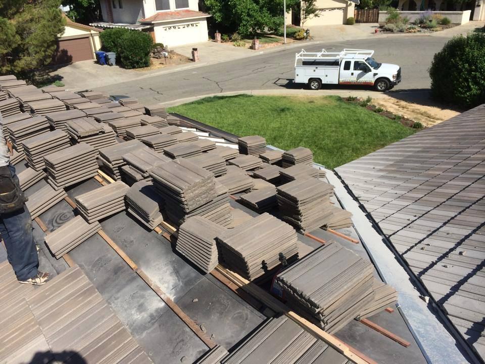 Tile stacked across a roof with a Sunrise Roofing service truck on the street below