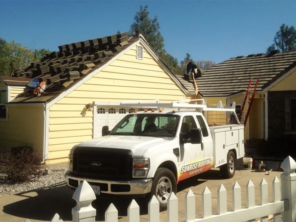 Sunrise Roofing truck parked at a home mid-reroof with crew on the roof