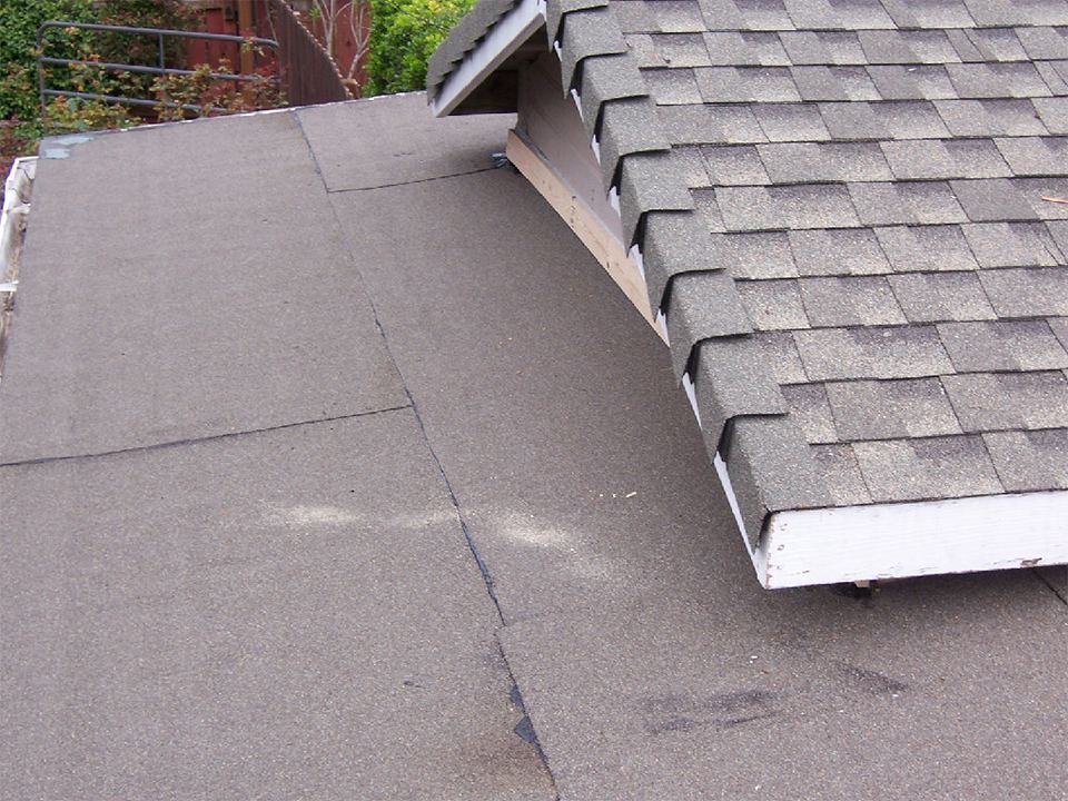 Composition shingles being installed over new underlayment at a dormer